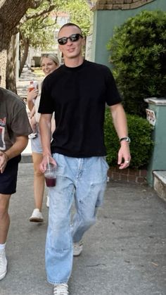 two men are walking down the street with drinks in their hands and one is wearing sunglasses