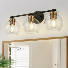 three light bathroom fixture with clear glass globes and brass accents on the vanity mirror