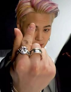 a close up of a person with pink hair and two rings on their fingers in front of the camera