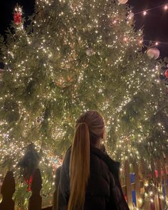 a woman standing in front of a large christmas tree with lights on it's branches