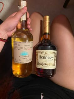 a woman is holding a bottle of hennessy and another bottle of brandy on her lap