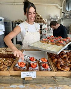 a woman in an apron is cutting strawberries on top of pastries at a bakery