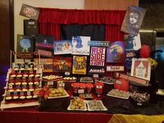 a table topped with lots of desserts and pastries next to a red curtain