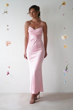 a woman wearing a pink dress standing in front of a wall with flowers on it