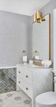 a bathroom with marble counter tops and gold accents on the mirror above the vanity, along with a white toilet