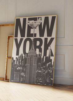 a framed new york poster sitting on top of a wooden floor in front of a white wall