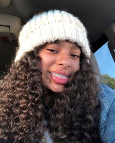 a woman with long curly hair wearing a white knitted hat in the back seat of a car