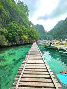 a long wooden dock extending into the water with boats docked on both sides and green mountains in the background