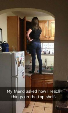 a woman standing on top of a refrigerator in a kitchen