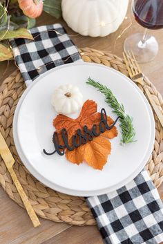 a white plate topped with an orange and black leaf next to a glass of wine