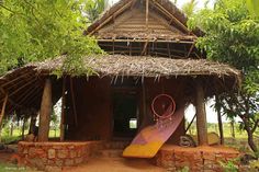 a small hut with a thatched roof and some decorations on the front porch, surrounded by trees