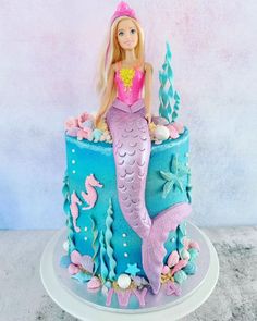 a barbie doll sitting on top of a blue and pink cake with sea creatures around it