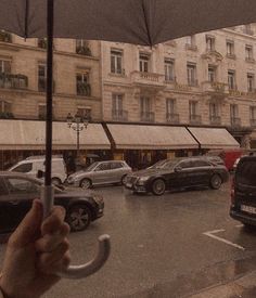 a person holding an open umbrella in front of a parking lot filled with parked cars