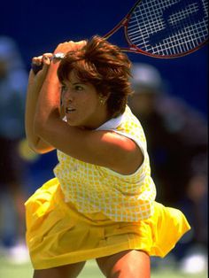 a woman holding a tennis racquet on top of a tennis court with people in the background