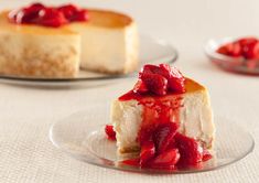 a cheesecake with strawberries is on a plate next to another piece of cake