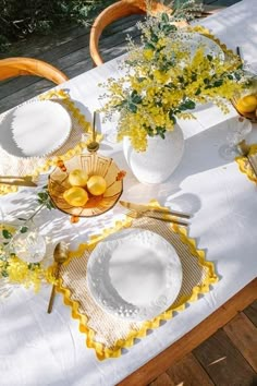 the table is set with yellow flowers and plates