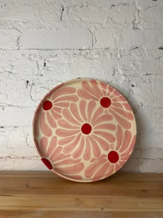 a pink and red plate sitting on top of a wooden table next to a white brick wall