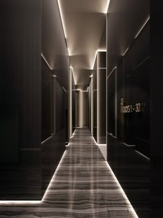 an empty hallway with black walls and wood flooring is lit by recessed lighting