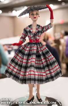 a doll wearing a dress and hat on display in a store or showroom with people walking around