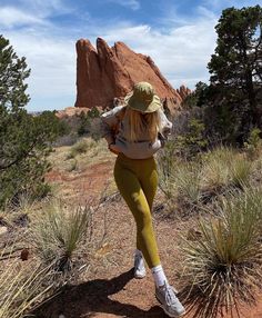 a woman in yellow pants and hat walking through the desert