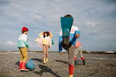 three people standing on the beach with surfboards in their hands and one holding a skateboard