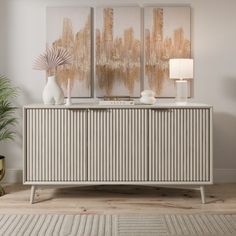 a sideboard with two paintings on it and a lamp next to it in a room