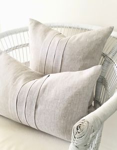 two gray pillows sitting on top of a white chair next to a basket filled with blankets