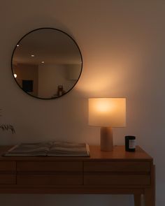 a table with a lamp and a mirror on the wall above it that has a book in front of it