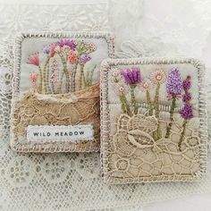 two embroidered coasters with flowers on them sitting on a lace doily covered tablecloth