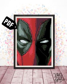 the deadpool cross stitch pattern is displayed in a frame on a wooden floor with confetti sprinkles behind it