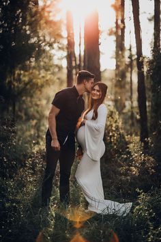 a man and woman are standing in the woods with their arms around each other as they kiss