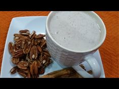 a white plate topped with a cup of coffee next to some pecans and cinnamon sticks