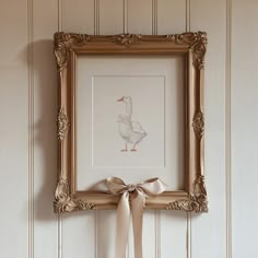 a white duck with a bow hanging on a wall in front of a framed painting