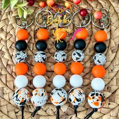 an assortment of orange, white and black beaded key chains on a woven basket