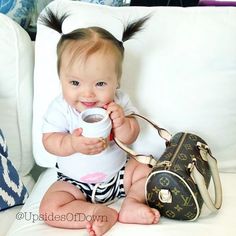 a baby sitting on a couch with a purse and coffee cup in her hand,