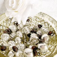 a glass bowl filled with christmas ornaments and a white rose