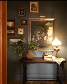 a room with pictures on the wall and a table in front of it next to a lamp