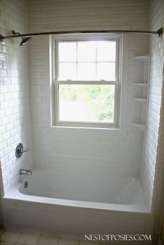 a bath tub sitting under a window next to a tiled floor and white tile walls