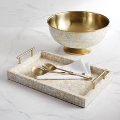 a golden bowl and silverware are on a marble tray with gold handles, along with a napkin holder