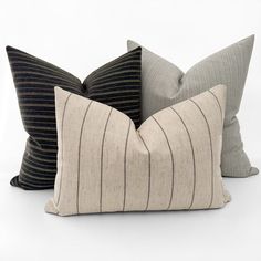 three pillows with black and white stripes are on a white surface, one is made out of fabric