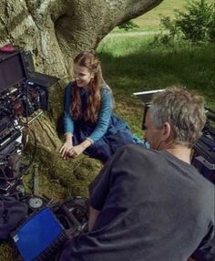 a man and woman sitting next to each other in front of a tree with cameras