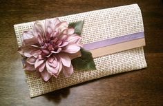 a pink flower is on top of a white piece of paper with purple ribbon and green leaves