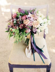 a bouquet of flowers sitting on top of a chair with purple ribbon around the back