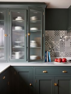 a kitchen with dark green cabinets and white counter tops, gold pulls on the glass doors