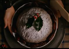 a person holding a cake with holly leaves on it and powdered sugar in the middle