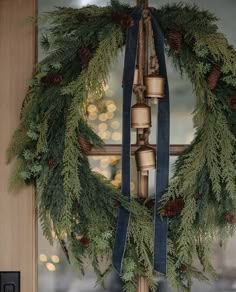 a christmas wreath with bells and pine cones hanging from it's side on a door