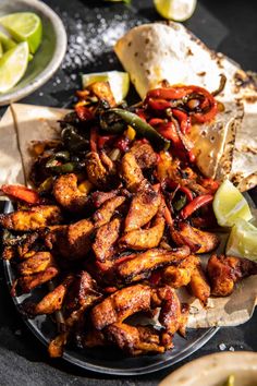 a plate full of chicken and peppers with tortilla wrappers on the side