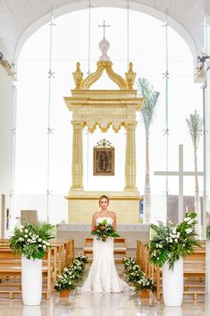 a woman standing in front of a church alter with flowers on the altar and greenery