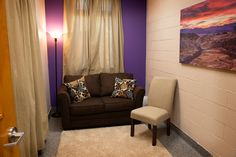 a living room with purple walls and a brown couch next to a window covered in curtains