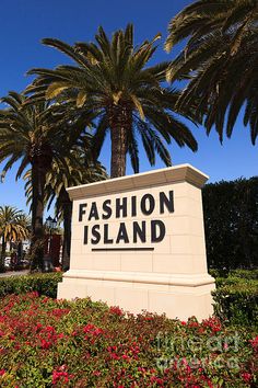 a sign that says fashion island in front of some palm trees and red flowered bushes